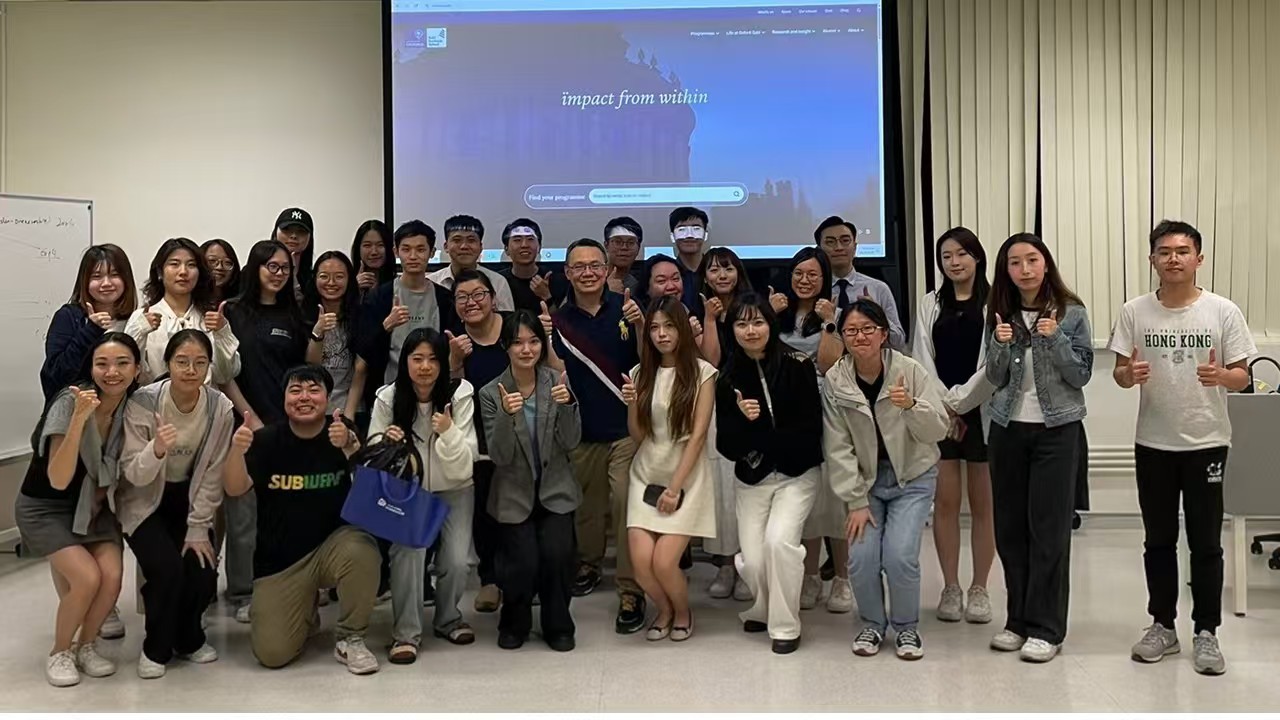 港大课堂上全班合影，众人竖起拇指，背后投影幕显示 impact from within
